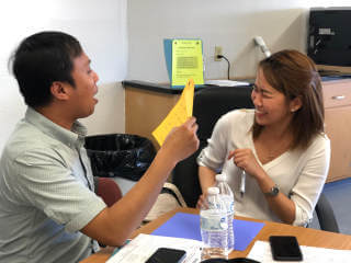 Man reading sheet while woman sitting across smiles
